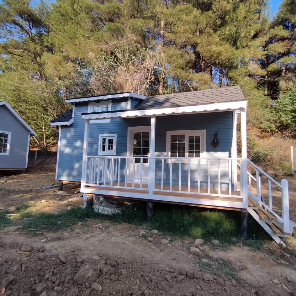 Ahşap tiny house — mavi cephe, beyaz söve ve ön veranda