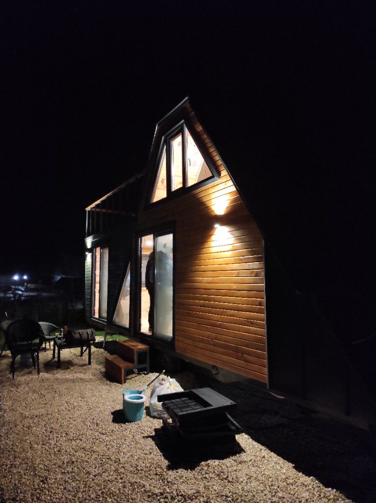 Ahşap tiny house — gece cam giriş ve loft üçgen pencere
